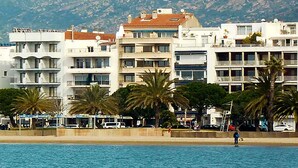 Un edificio costero con varios balcones, una playa de arena y palmeras.