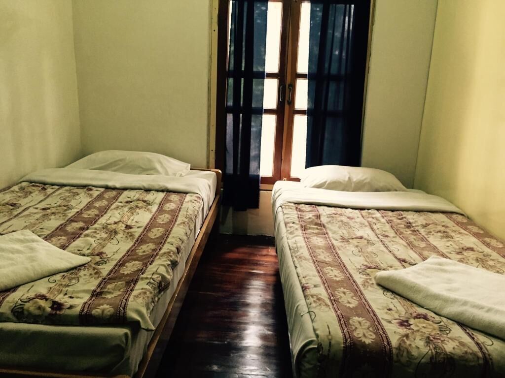 Habitación con dos camas individuales, piso de madera y ventana con cortinas.