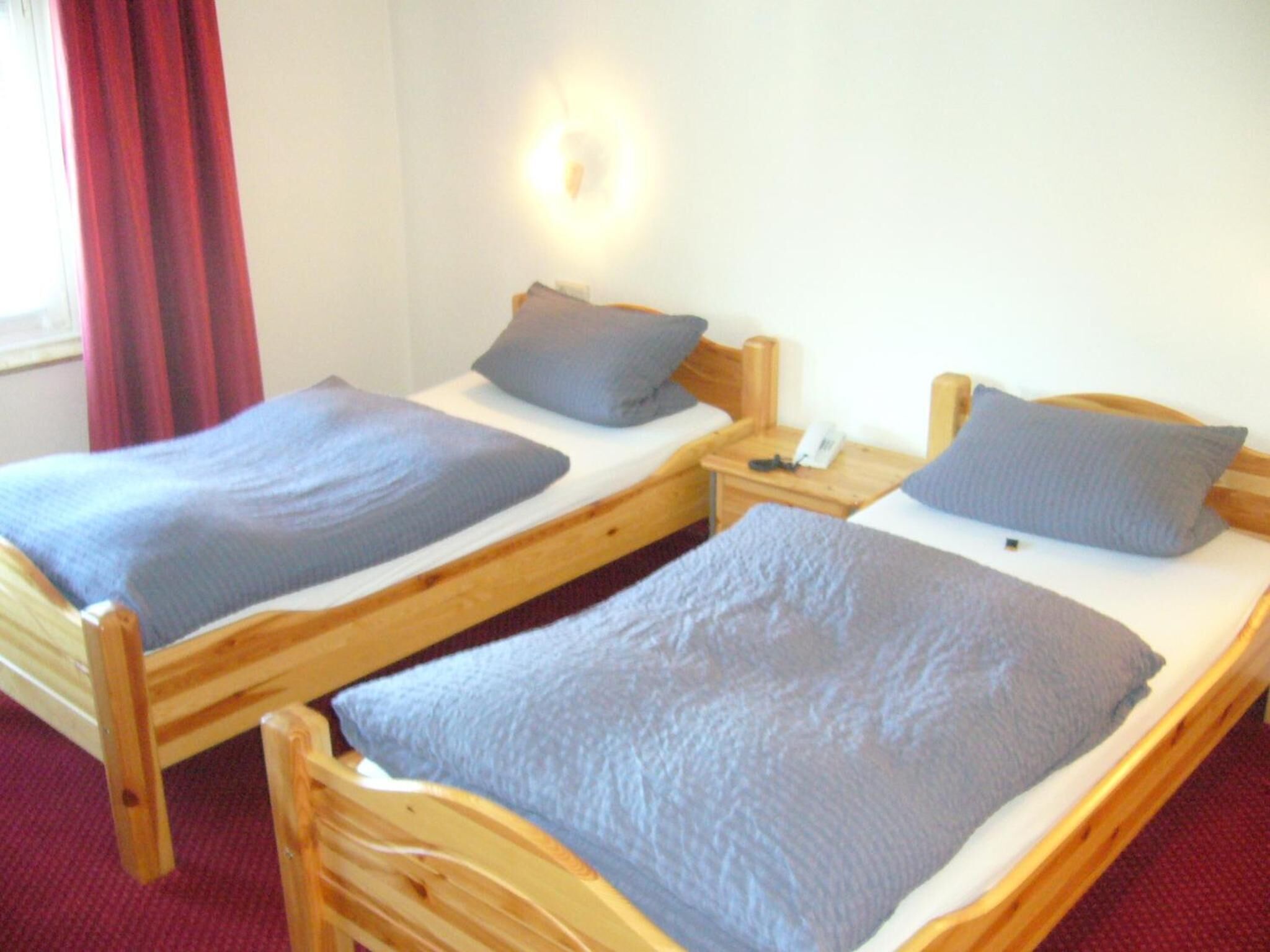 Two wooden beds with grey bedding and a nightstand with a telephone.