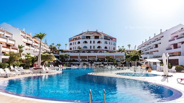 A large swimming pool surrounded by lounge chairs and umbrellas, with a multi-story building in the background. - Parque Santiago 1: Seafront apartment with private terrace & £100K pool makeover (Costa Adeje)