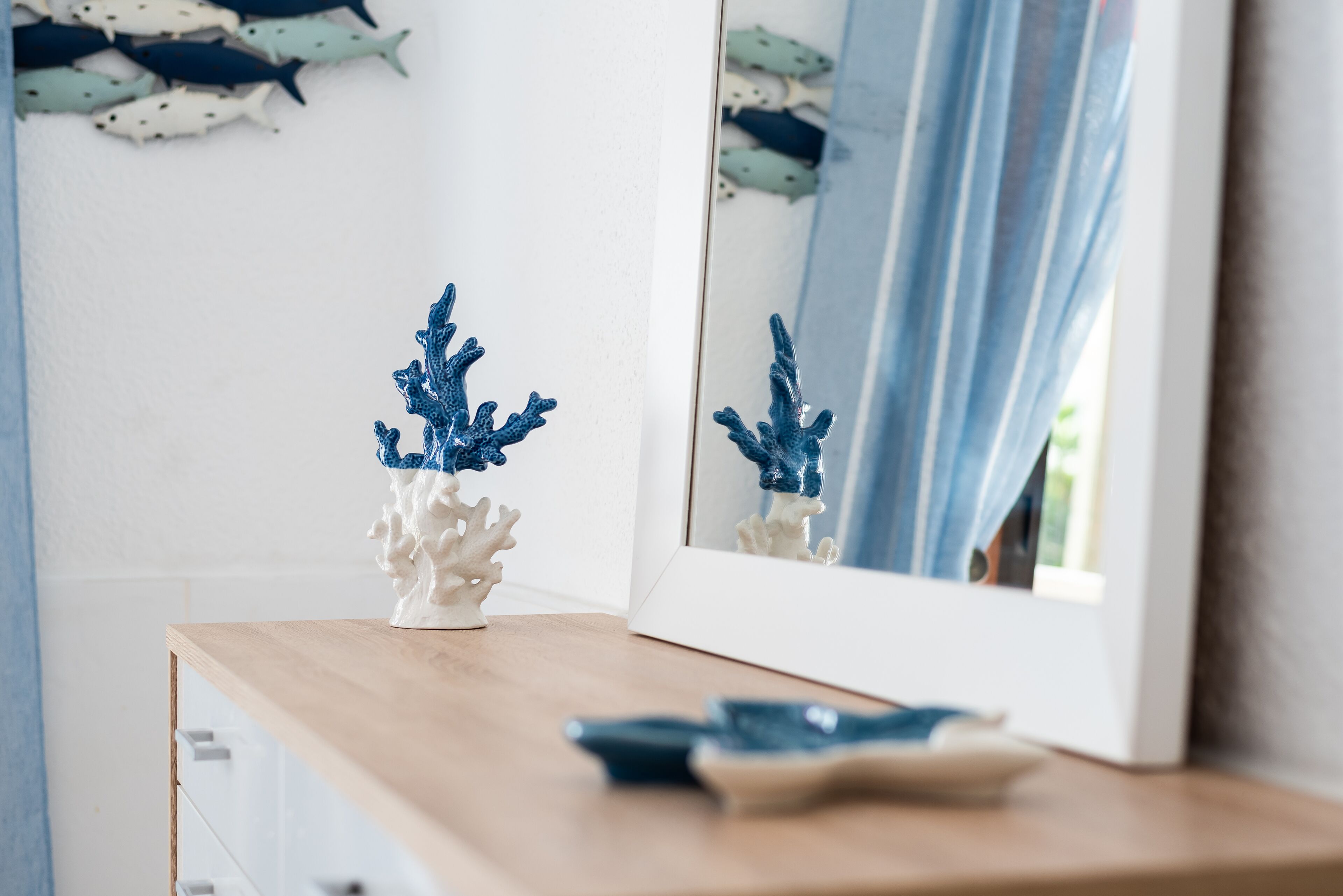A wooden dresser with a white vase and a blue coral decoration.