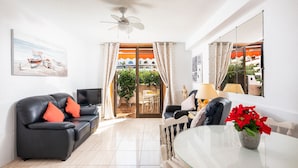 A living room with a black leather sofa, a glass dining table, and a ceiling fan. - Parque Santiago 1: Seafront apartment with private terrace & £100K pool makeover (Costa Adeje)