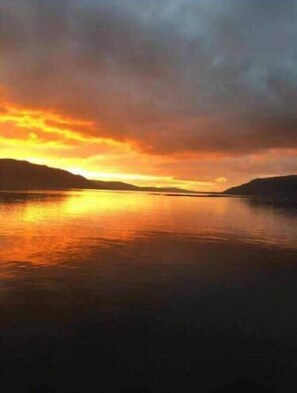Un atardecer sobre aguas tranquilas, con colinas al fondo.