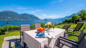 A table set outdoors with a view of mountains and a lake, a book, and a bowl of fruit. - Casa Laura Apt. 3, Plesio, Italy (Plesio)