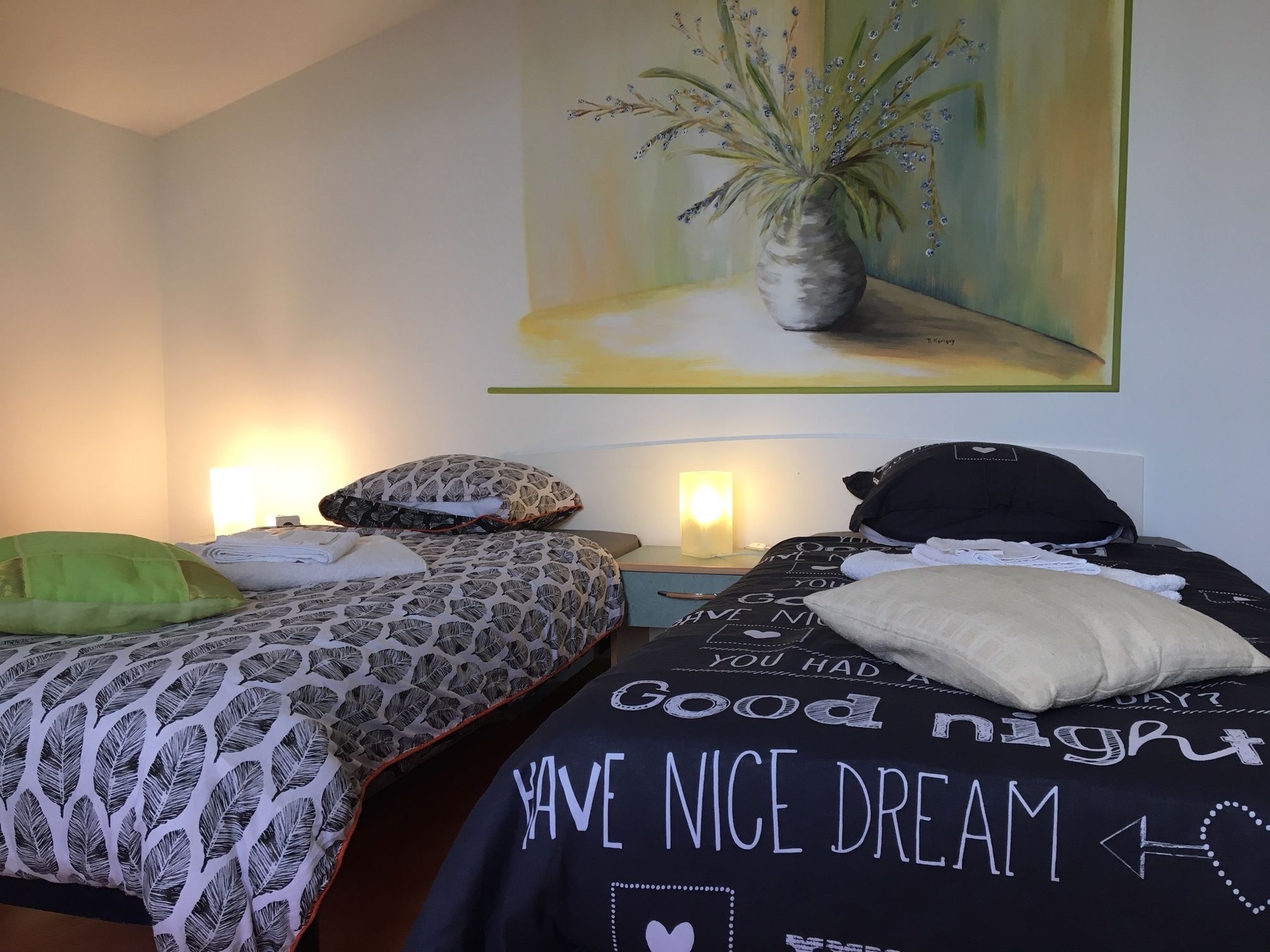 A hotel room with two beds, each with patterned bedding and pillows. There is a painting of a plant on the wall above the beds.
