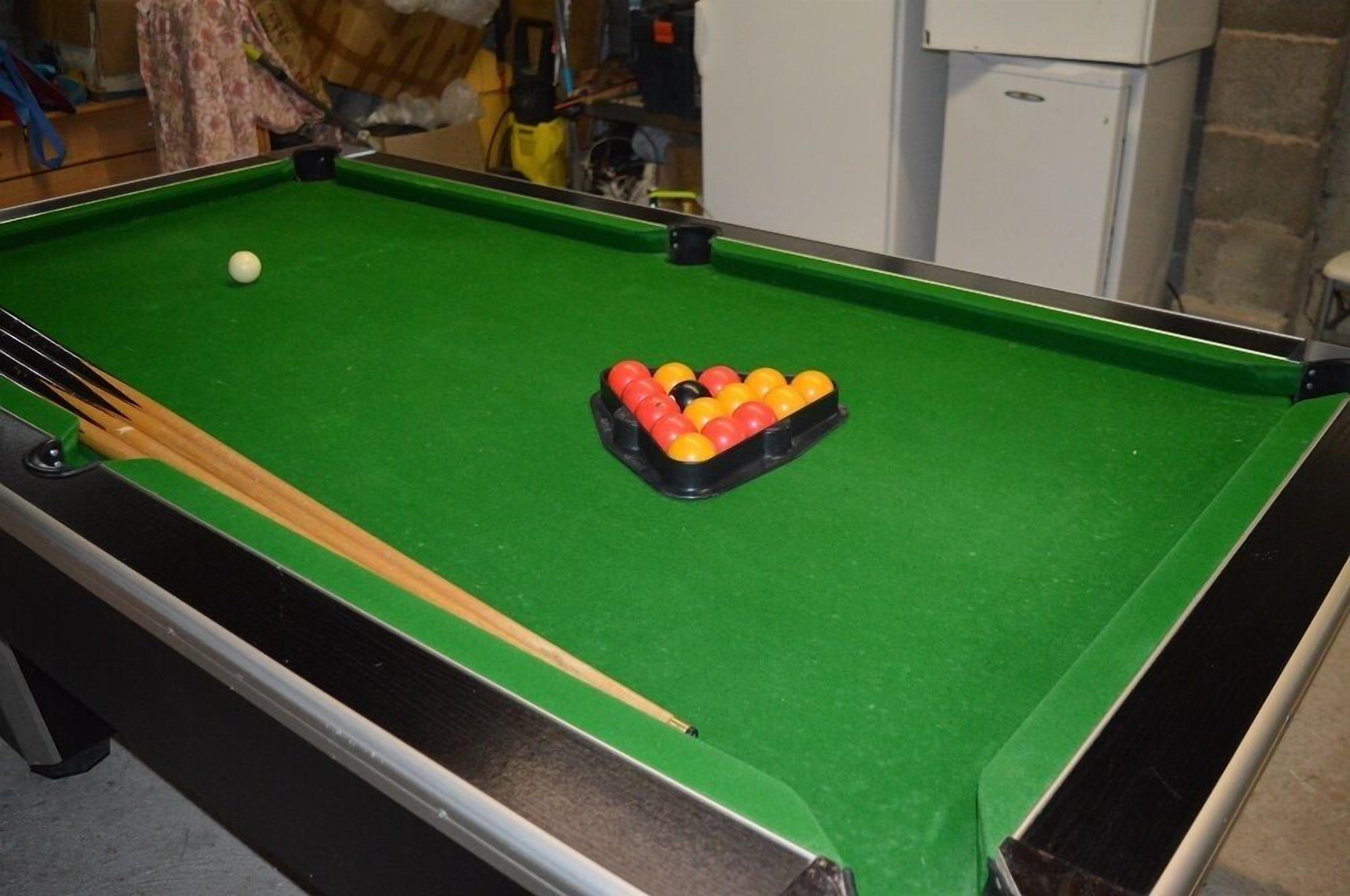 A pool table with a green felt surface, a cue stick, and a rack of billiard balls.
