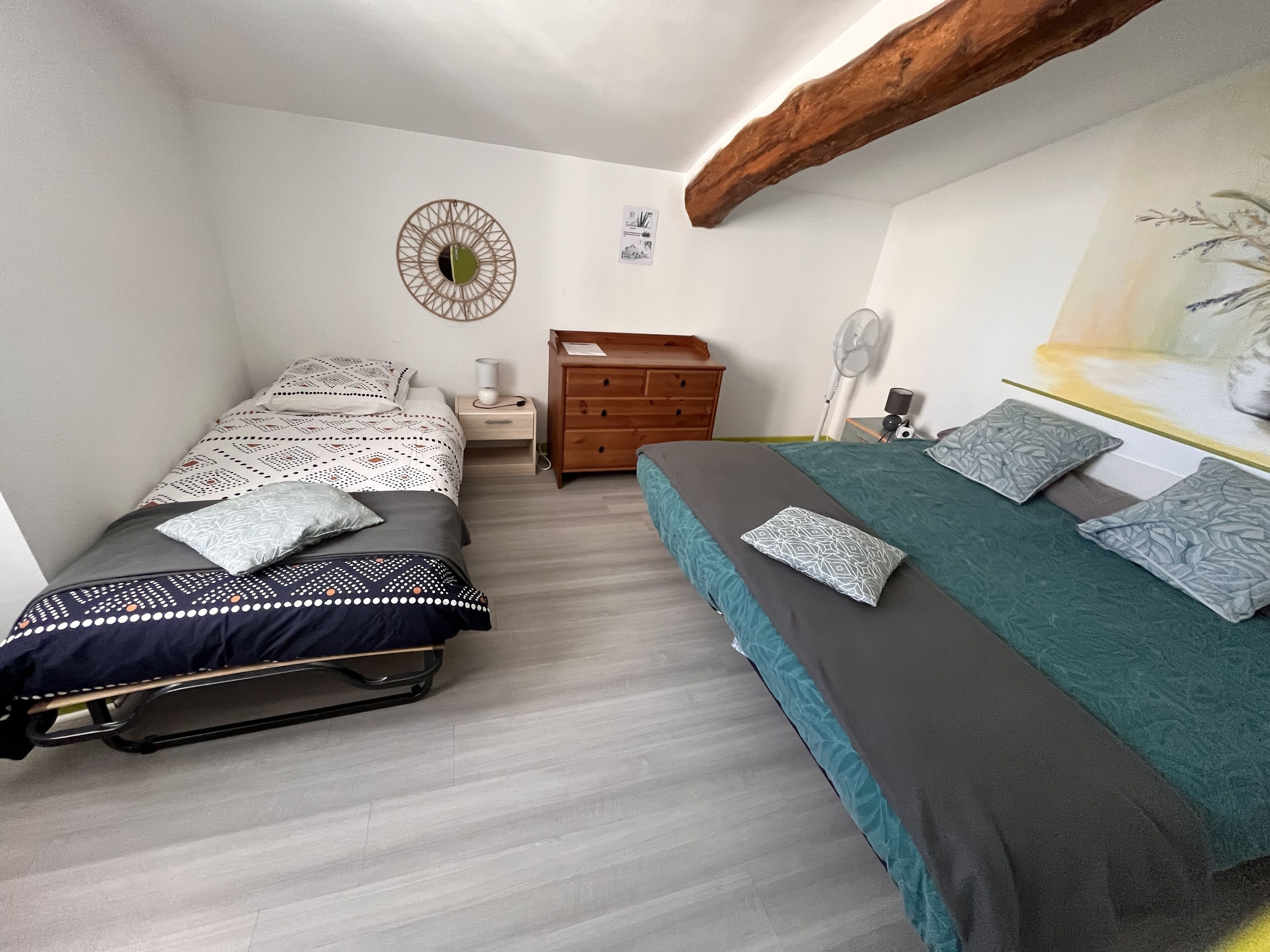 A bedroom with two beds, a wooden dresser, a wall clock, and a ceiling fan.