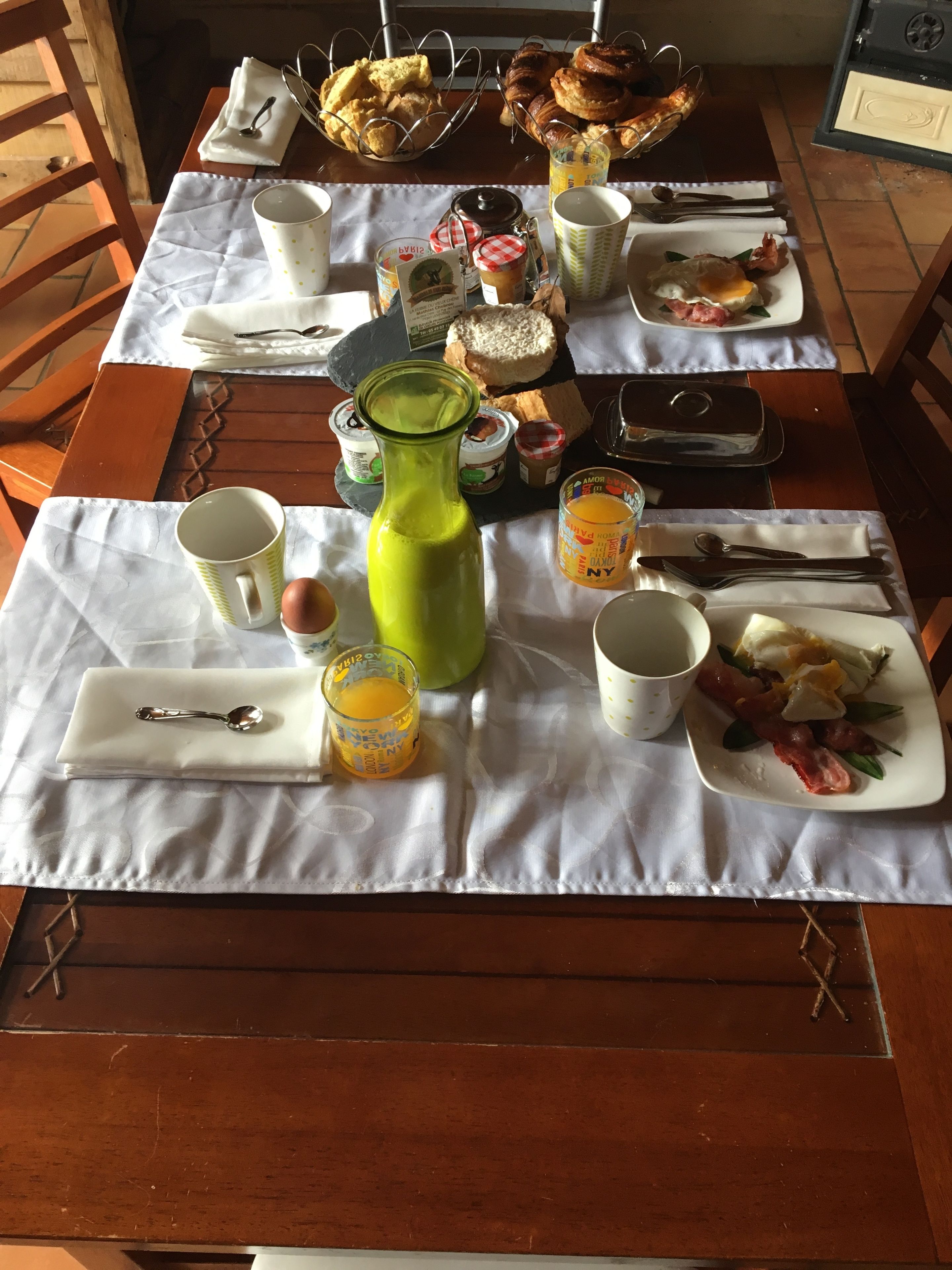 A breakfast table with various food items, utensils, and a green bottle.