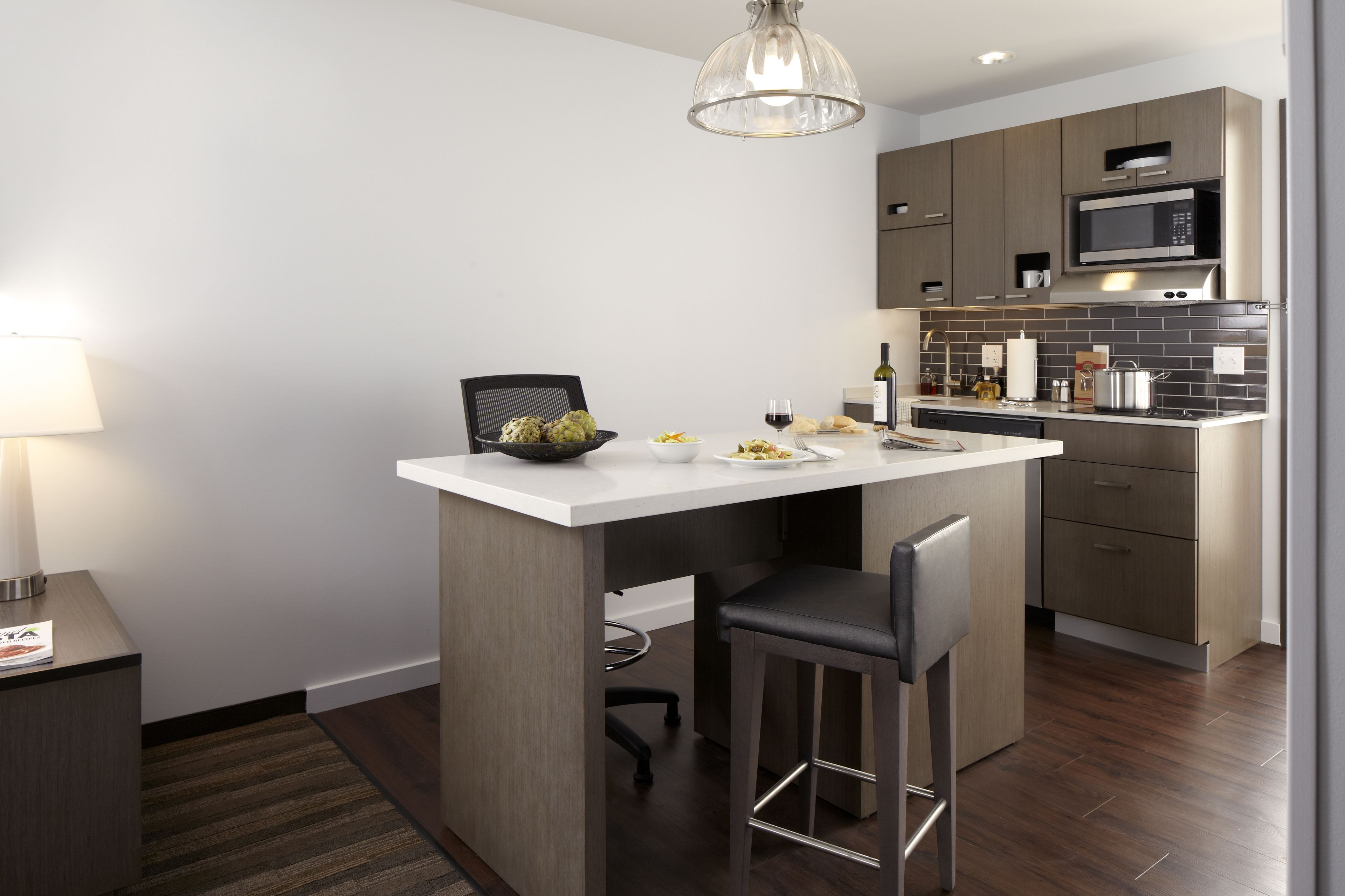 A modern kitchen with a central island, bar stools, a microwave, and a wine bottle.