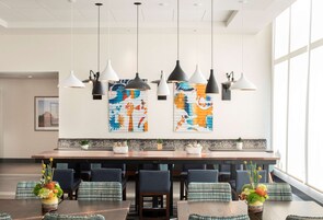 A modern dining area with a long wooden table, multiple chairs, and pendant lights.