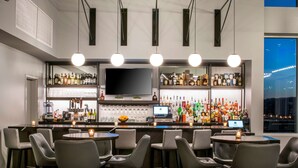 Un área de bar con diversas opciones de asientos, un televisor y una estantería repleta de licores.