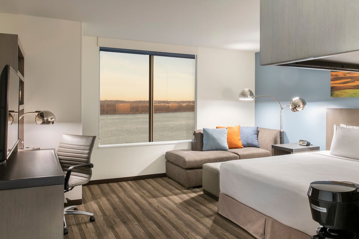 Une chambre d’hôtel équipée d’un lit, d’un bureau, d’une chaise, d’un canapé et d’une grande fenêtre donnant sur un plan d’eau.