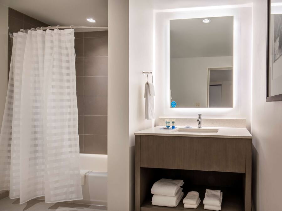 Un bagno moderno con tenda doccia, lavabo con specchio e asciugamani ordinatamente piegati su uno scaffale.