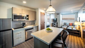 Una cocina moderna con electrodomésticos de acero inoxidable, una isla central y un área de descanso con televisor y lámpara.