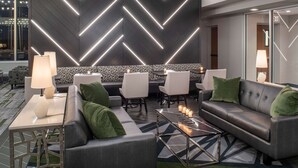 Un moderno vestíbulo de hotel con una pared de diseño geométrico, un sofá de cuero y una zona de comedor con sillas blancas y una mesa.