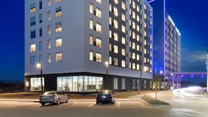 Un hotel moderno con varios pisos, ventanas amplias y un estacionamiento con automóviles.
