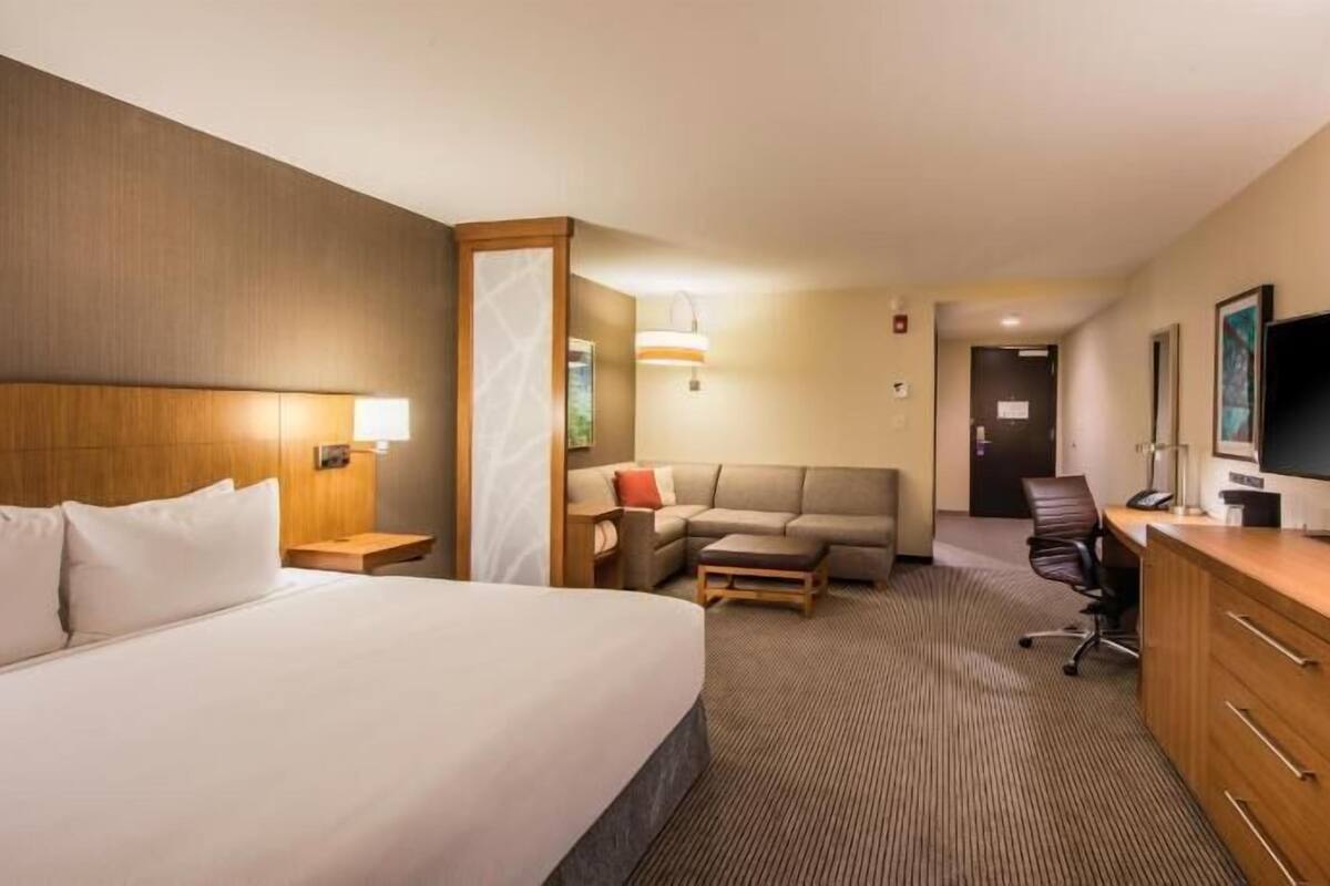 Ein Hotelzimmer mit Bett, Schreibtisch, Sessel, Sofa und Fernseher.