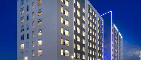 A modern hotel with multiple floors, large windows, and a parking lot with cars.