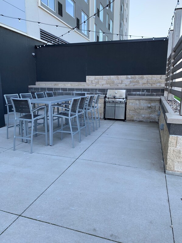 An outdoor patio with a grill, chairs, and a table. - Hyatt Place East Moline Quad Cities (East Moline)