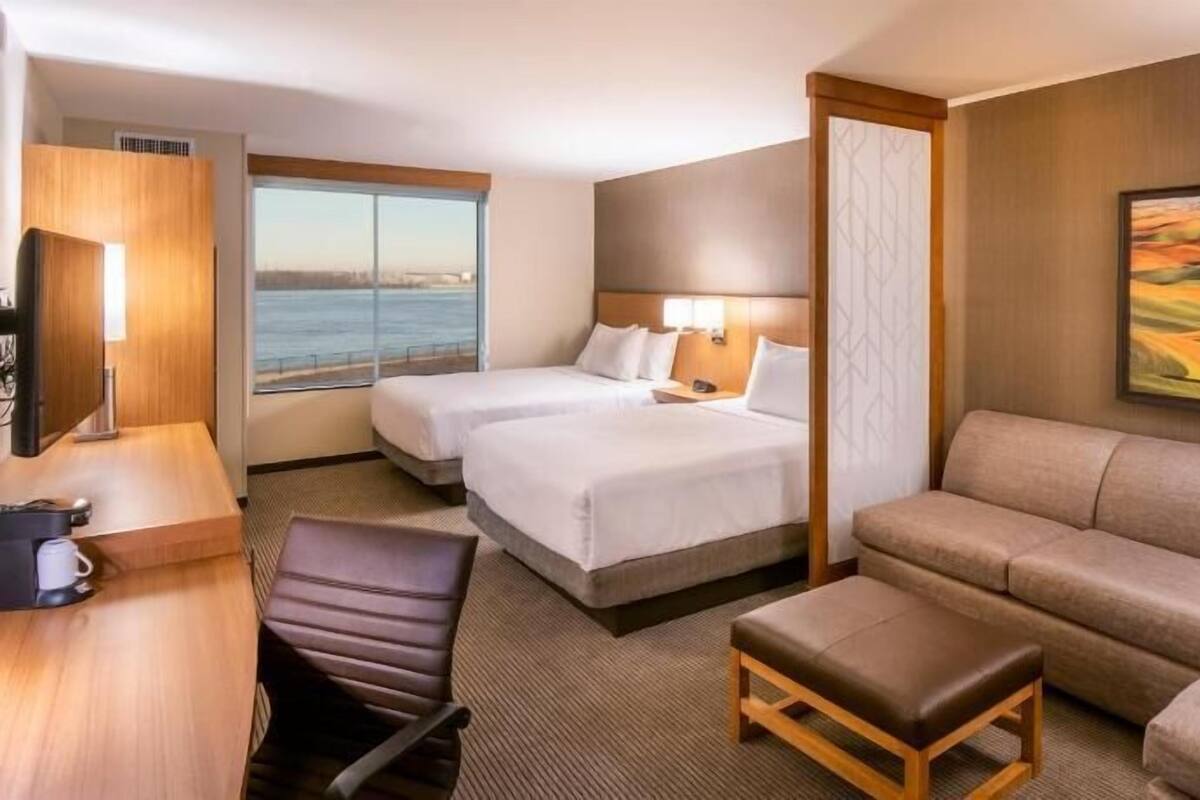 Ein Hotelzimmer mit zwei Betten, einem Schlafsofa, einem Schreibtisch, einem Stuhl und einem Bild an der Wand.