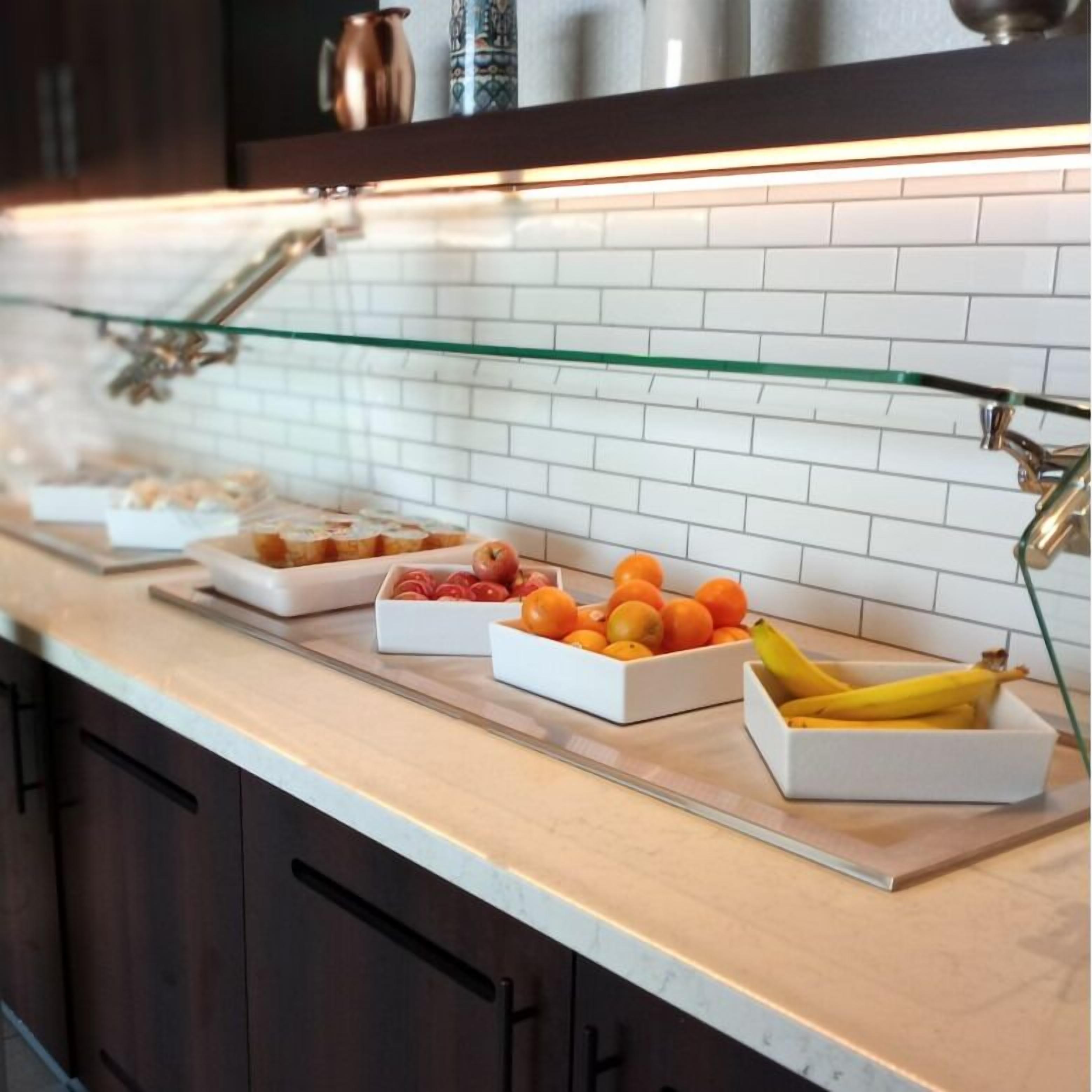 Una encimera de cocina con armarios de vidrio, salpicadero de azulejos blancos y diversos alimentos.