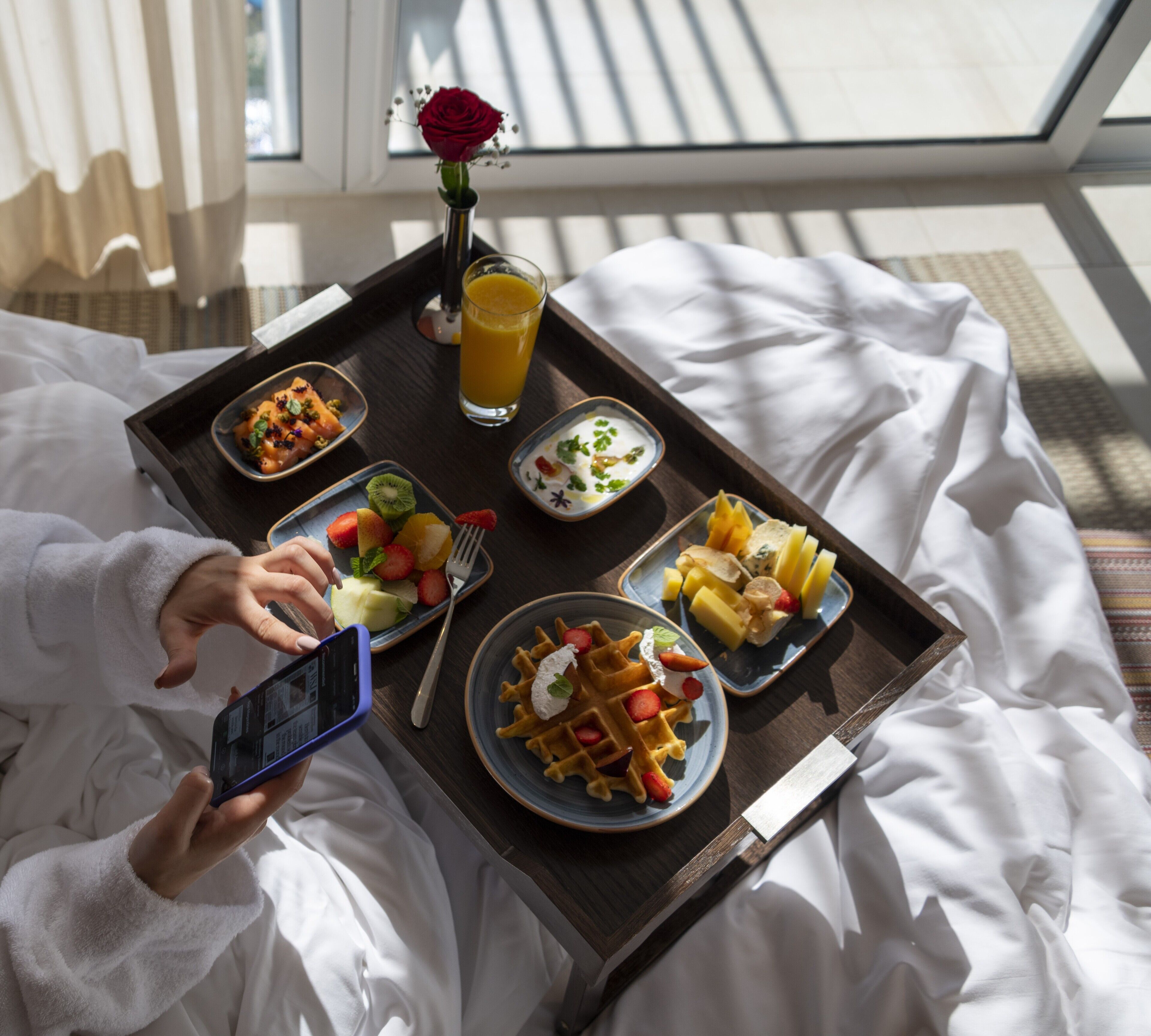 A breakfast tray with waffles, fruit, and a glass of orange juice on a bed.