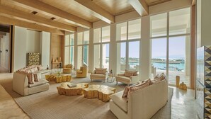 A spacious living room with large windows, a view of the sea, and modern furniture.