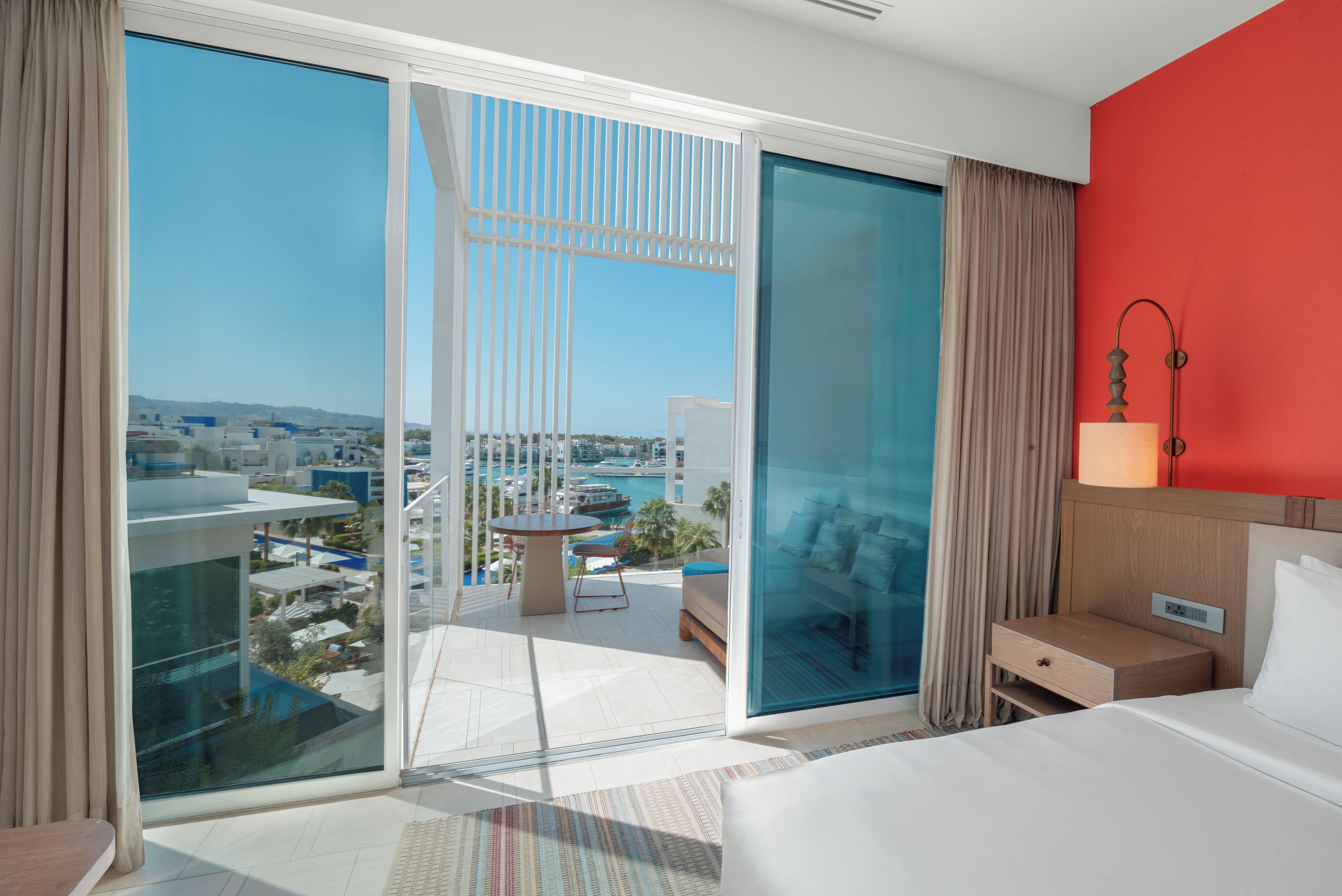 A hotel room with a large sliding glass door leading to a balcony with a city view.