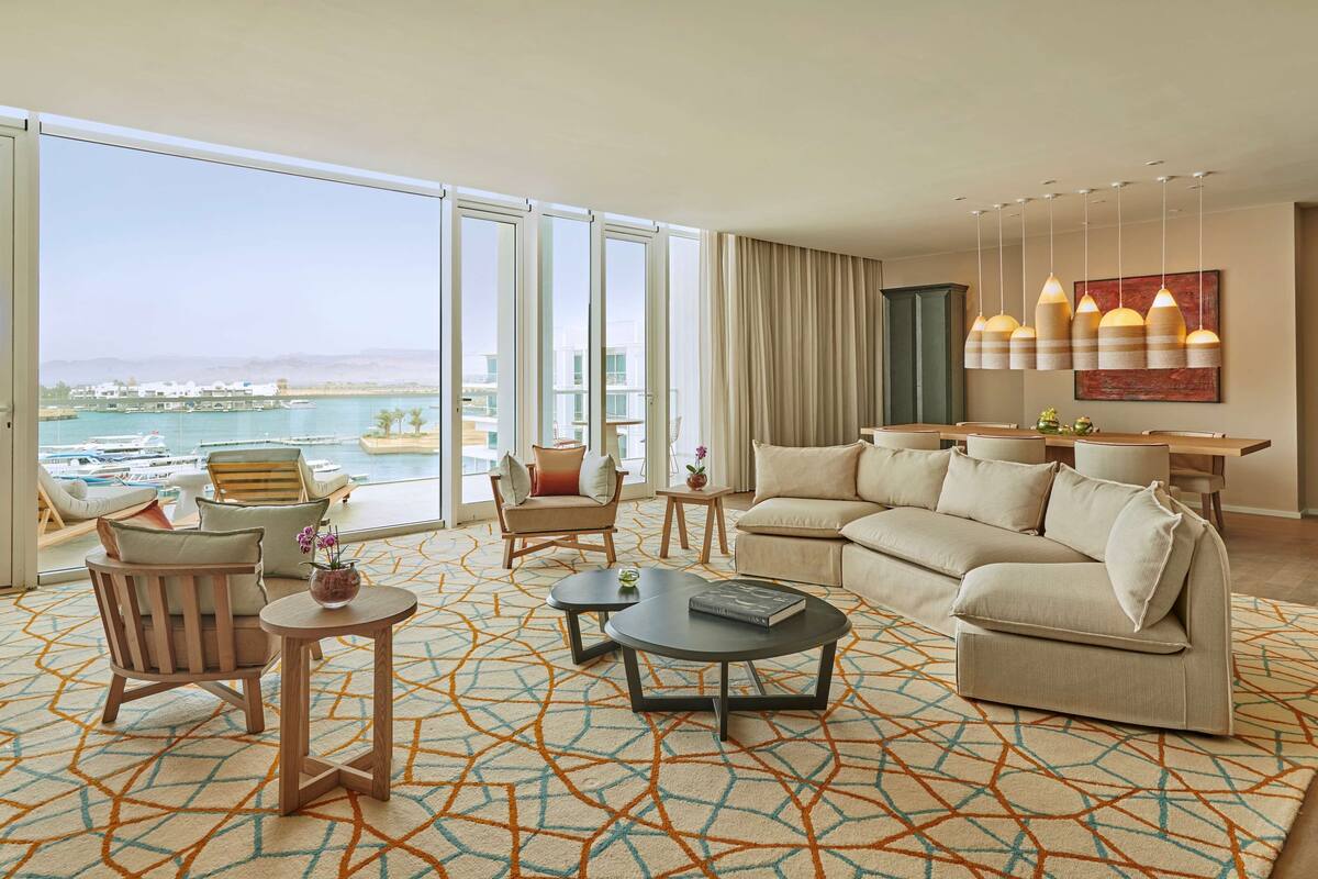A spacious living room with a large sofa, a coffee table, and a view of the marina through floor-to-ceiling windows.