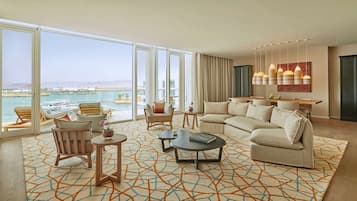 Un salón amplio con un sofá grande, una mesa de centro y vistas al puerto deportivo a través de ventanales de gran altura.