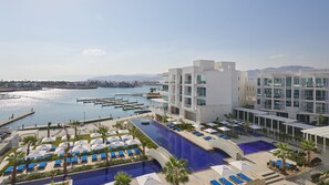 Un hotel moderno con piscina en la azotea, un puerto deportivo y vistas al mar.
