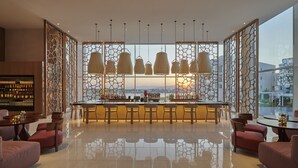 A modern bar area with a high bar, multiple hanging pendant lights, and a view of the sunset through a patterned glass wall. - Hyatt Regency Aqaba Ayla Resort (Aqaba)