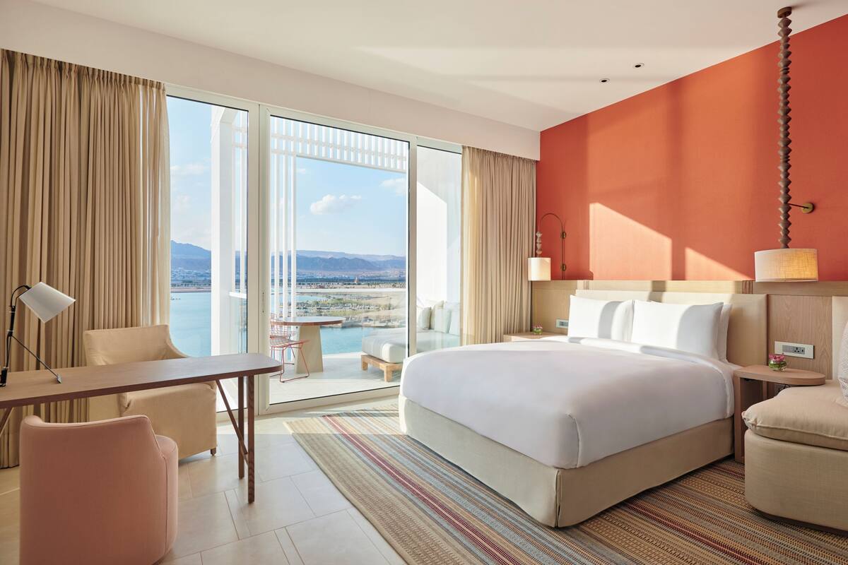 A hotel room with a large bed, a desk, a chair, a sofa, and a view of the sea.