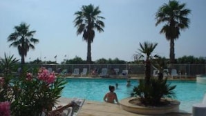 Zona de piscina con palmeras, sillas de descanso y cielo despejado.