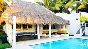 A poolside area with a thatched-roof structure, white walls, and colorful cushions.