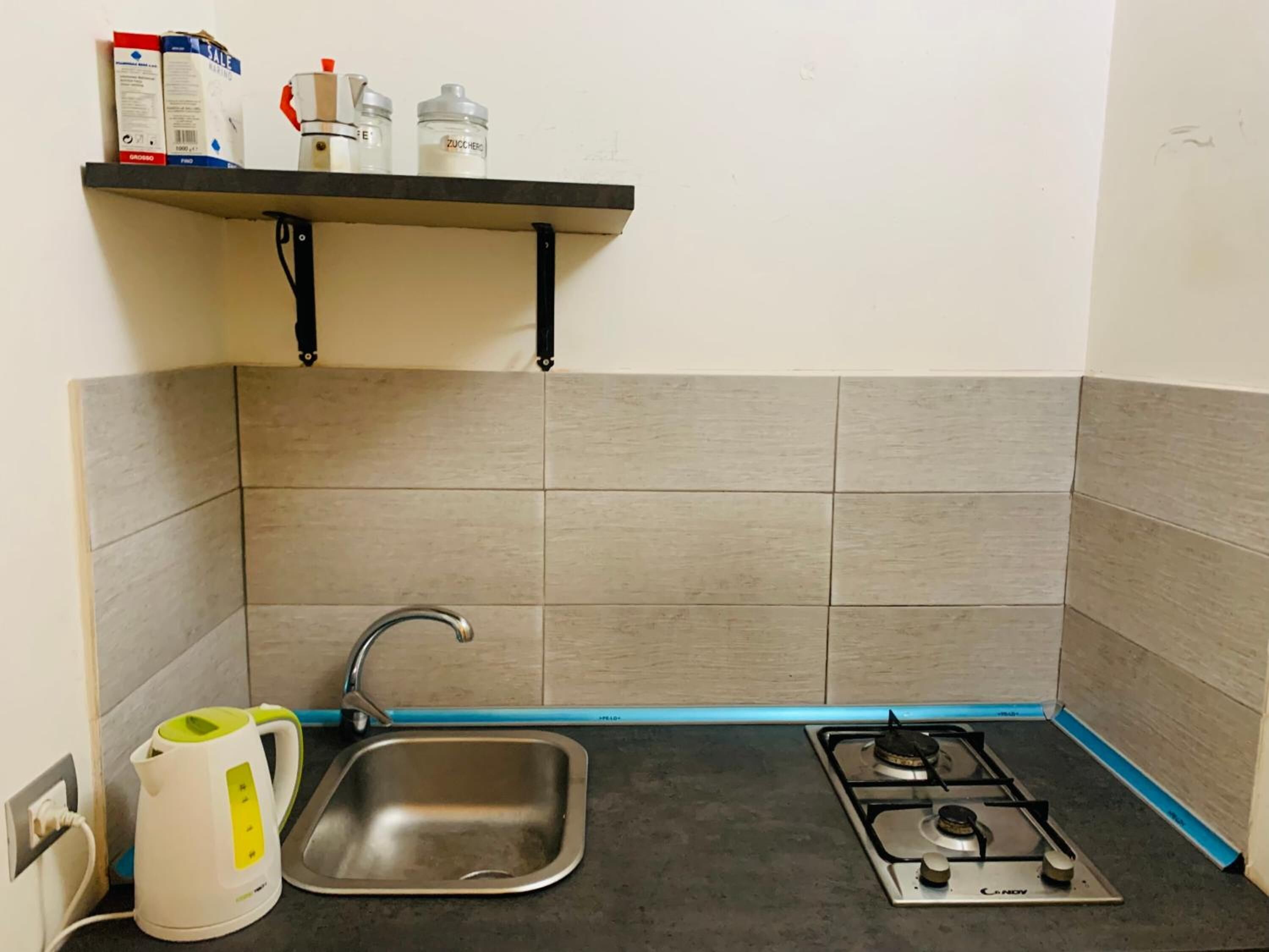 Una piccola cucina con lavandino, bollitore e piano cottura a gas.