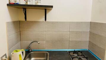 Una piccola cucina con lavandino, bollitore e piano cottura a gas.