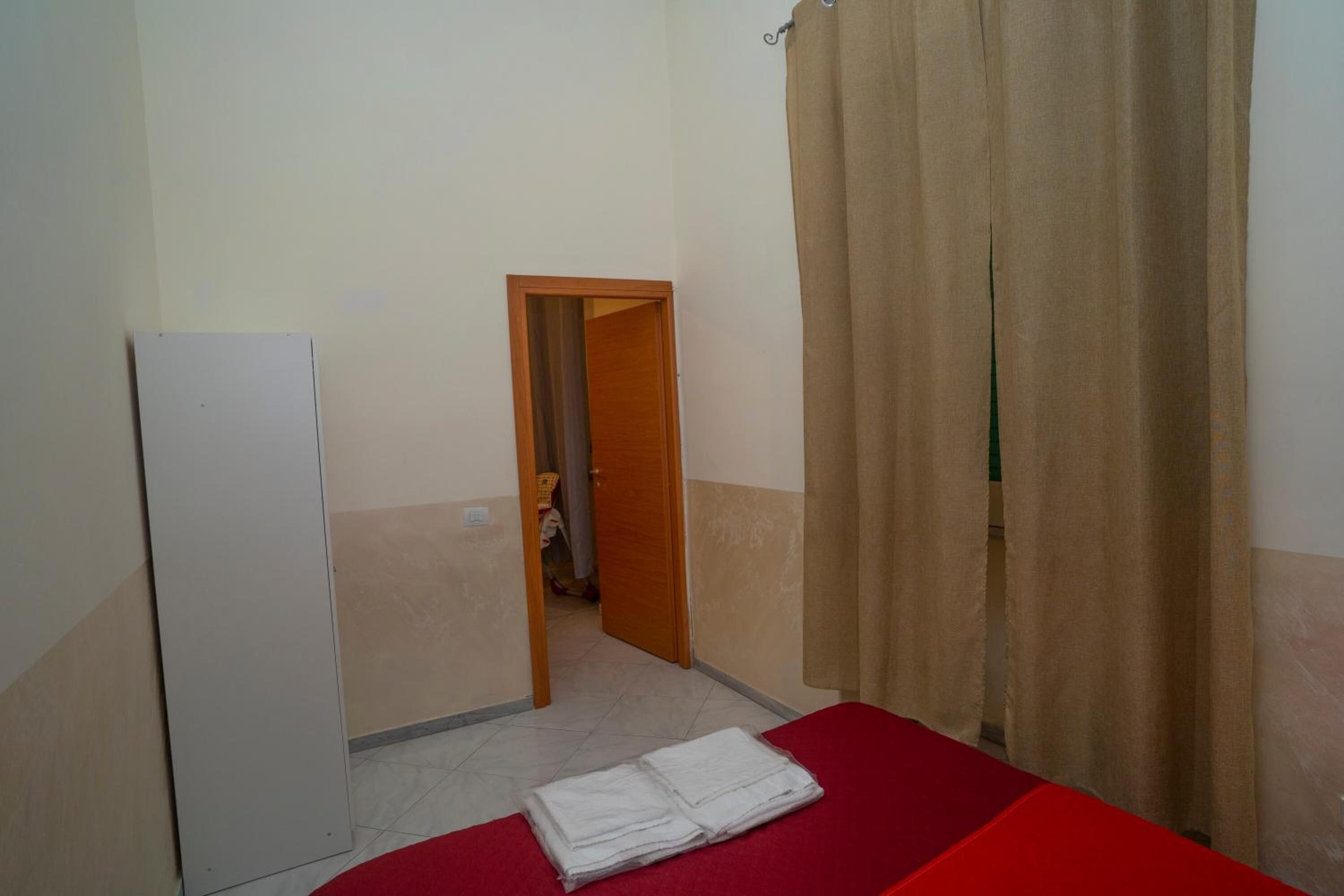 A small, simple room with a bed, a door leading to another room, and a curtain.