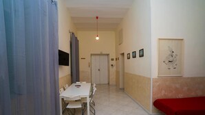 Una habitación con una mesa y sillas blancas, una cama roja y una puerta al fondo.