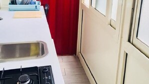 Una cocina con encimera blanca, una puerta roja y una ventana con persianas.