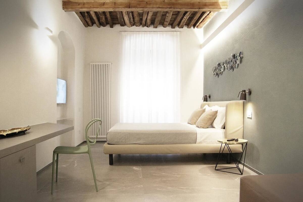Een slaapkamer met een bed, nachtkastje, stoel en een klein tafeltje met een lamp.