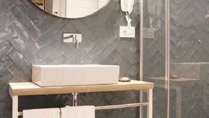 Een badkamer met een rechthoekig wastafelmeubel, een ronde spiegel en een douchecabine met glazen wanden.