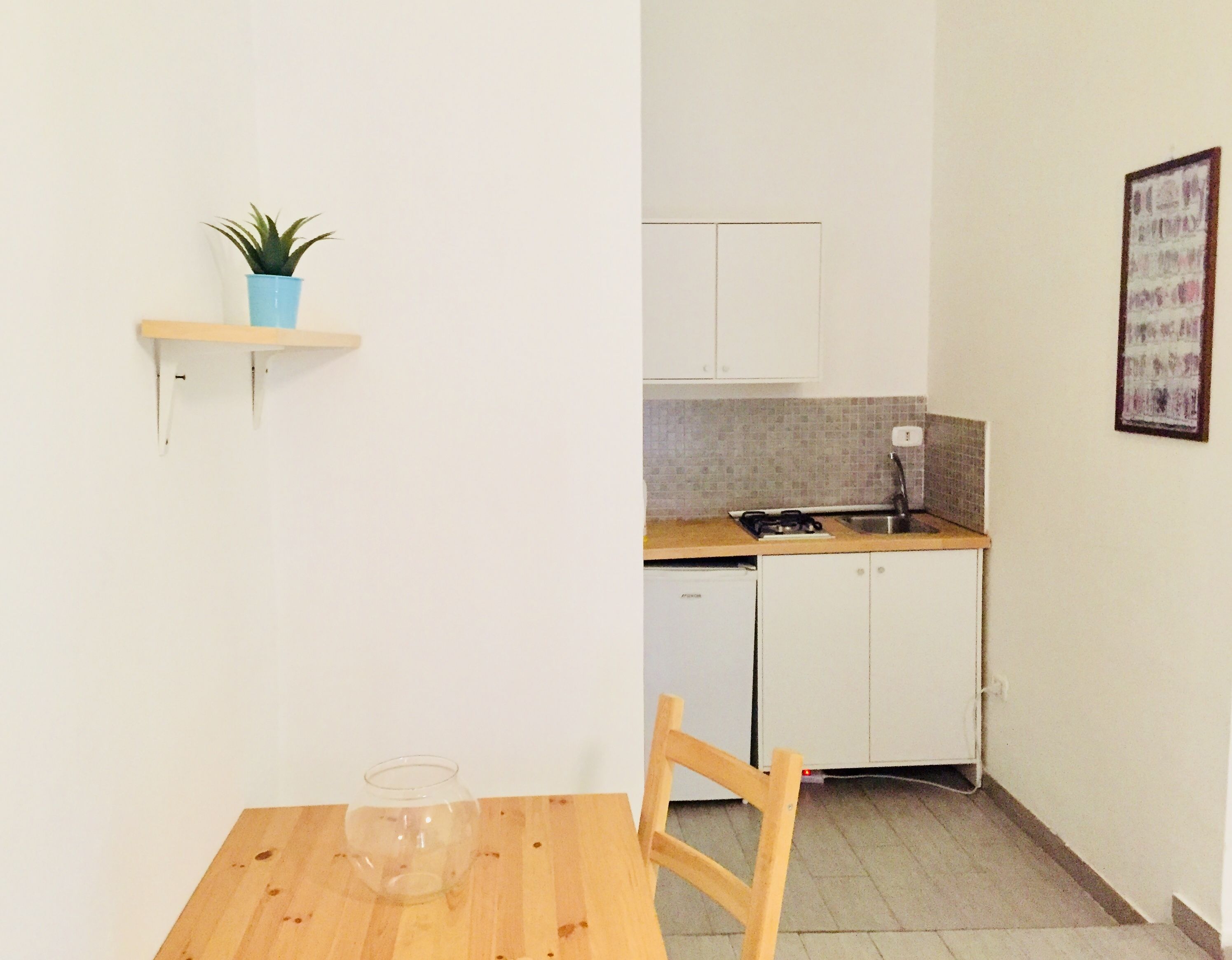 A small kitchen with a wooden table, a chair, a potted plant, and a dishwasher.