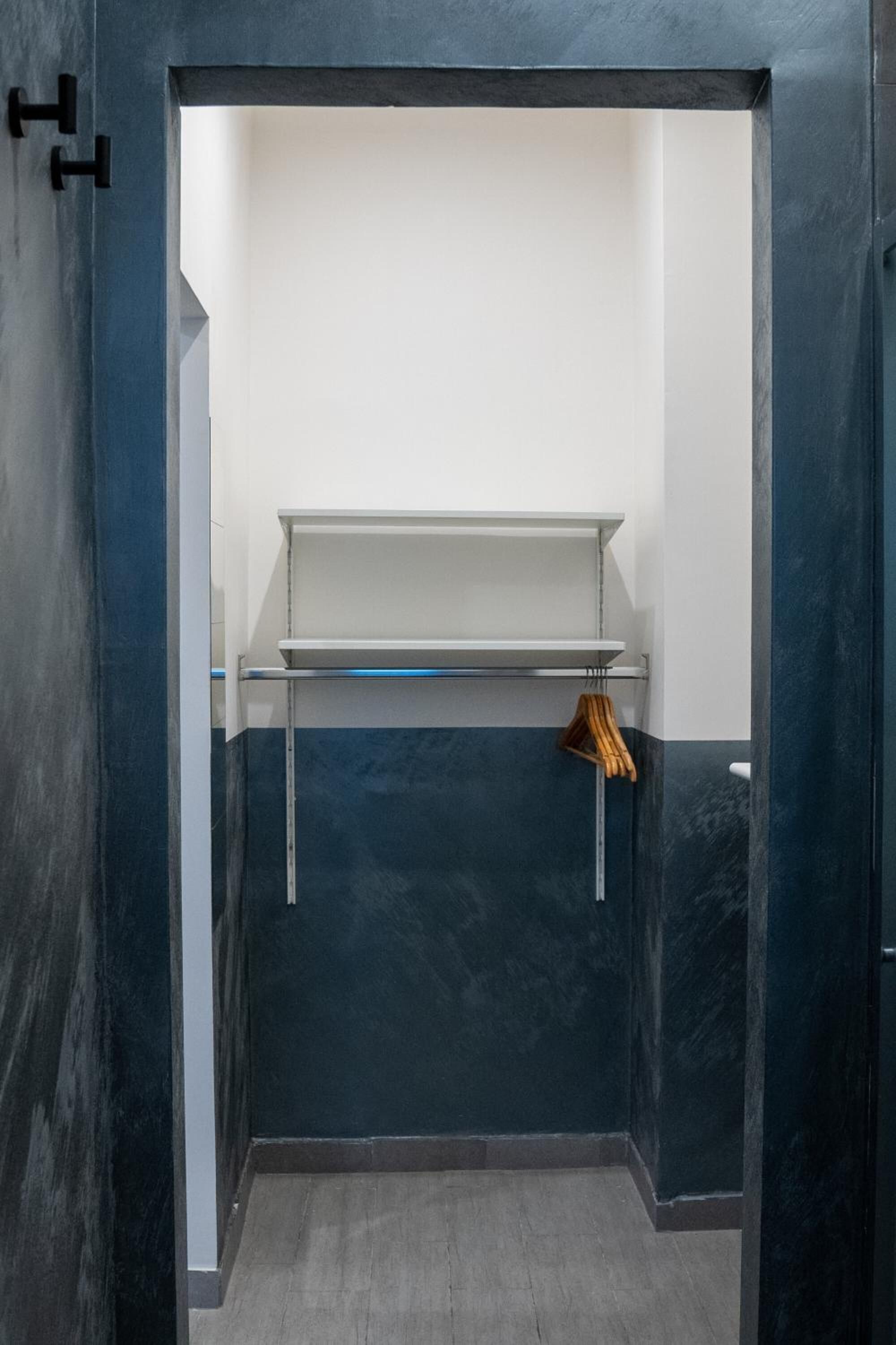 Ein kleines, abgeschlossenes Badezimmer mit dunkelblauer Wand, weißem Ablagebrett und Holzaufhänger.