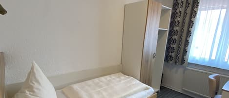 Habitación individual con una cama de madera, cabecera de madera, mesita de noche, armario y ventana con cortinas.