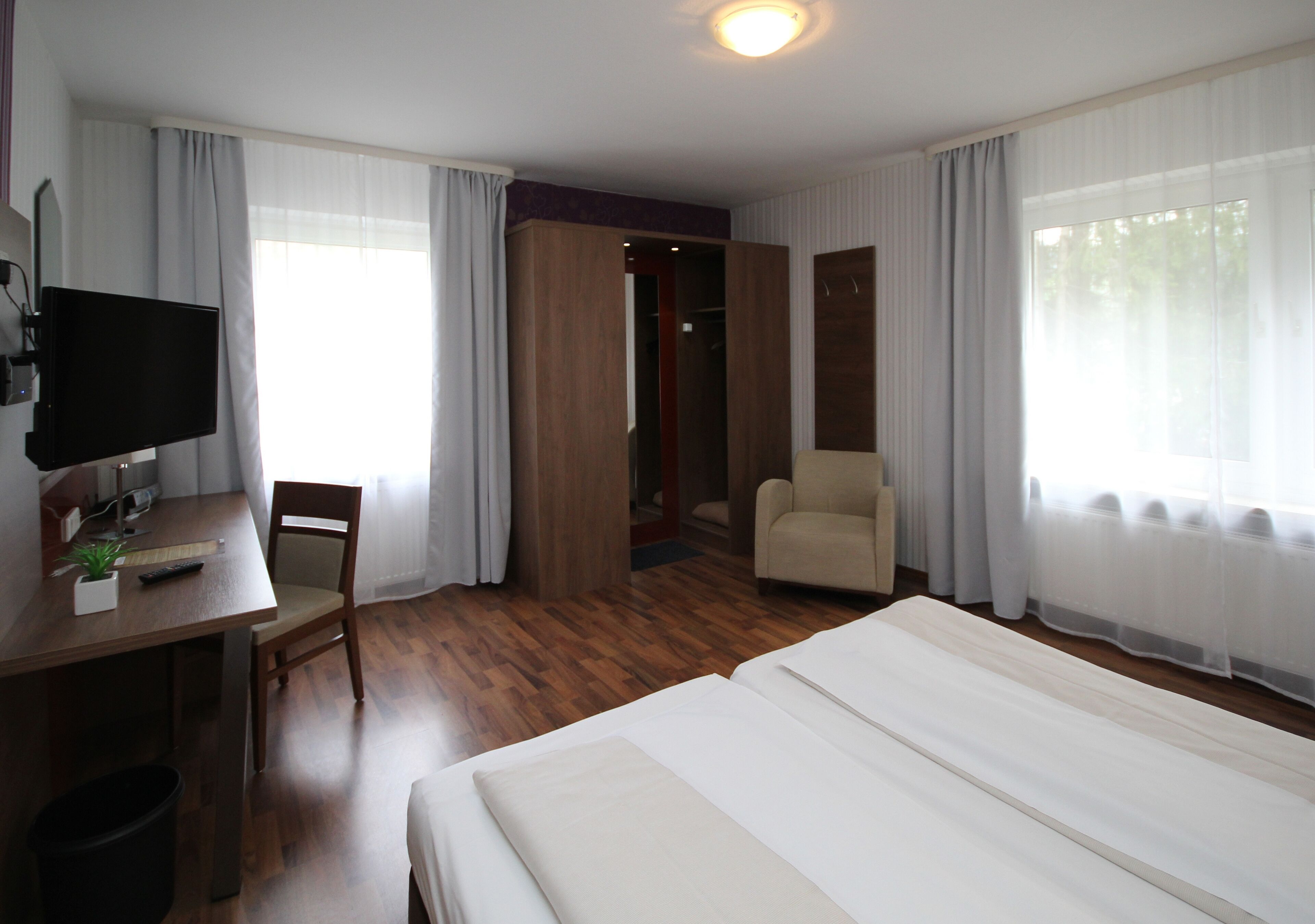 A hotel room with a bed, a desk with a chair, a television, and a wardrobe.