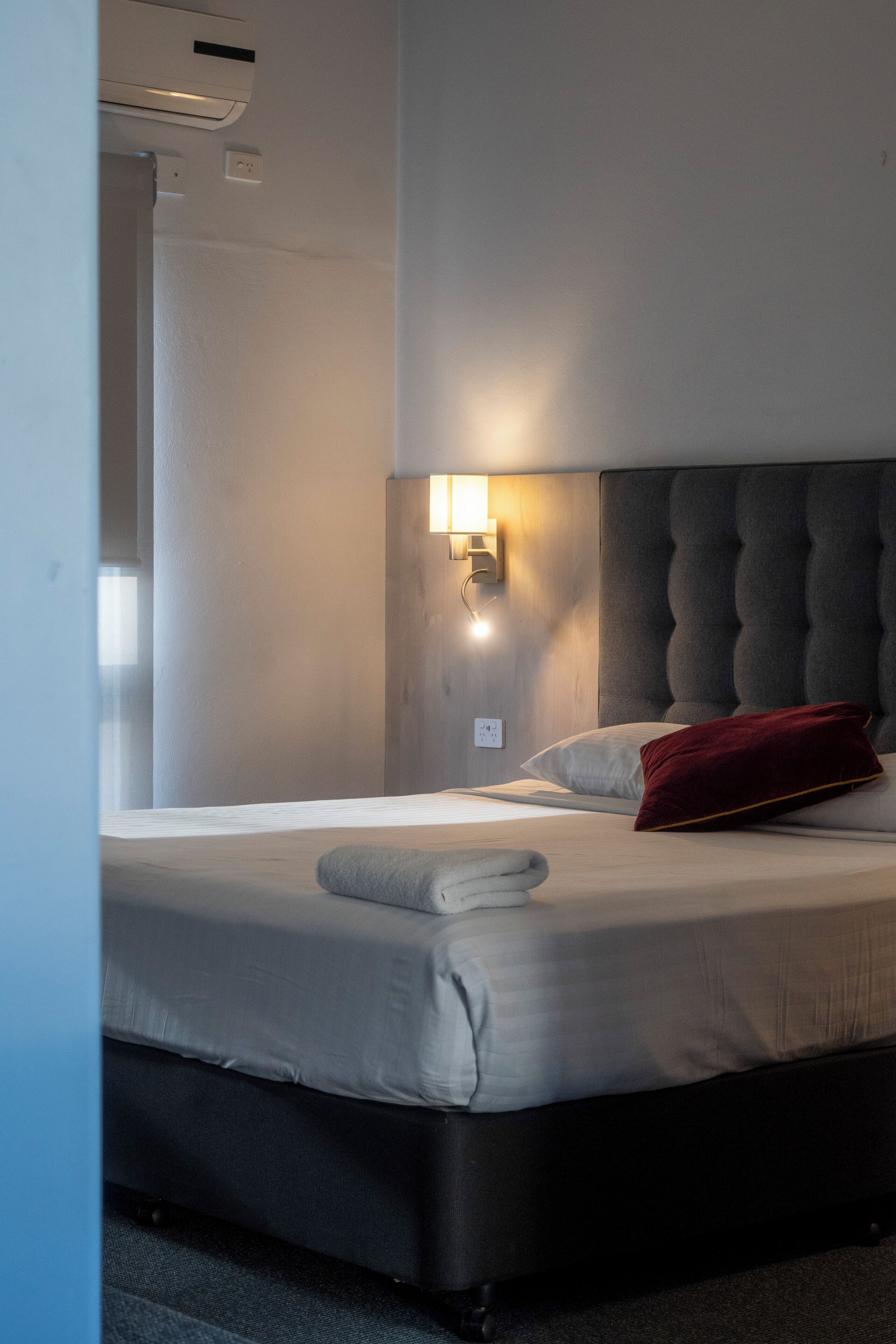Habitación de hotel con una cama, una luz fijada a la pared y un respiradero en el techo.