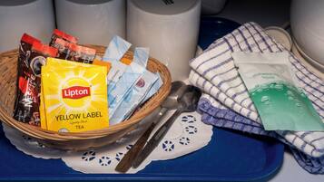 A basket with Lipton tea and coffee packets, a spoon, and a dishwashing liquid packet on a blue tray with a white doily.