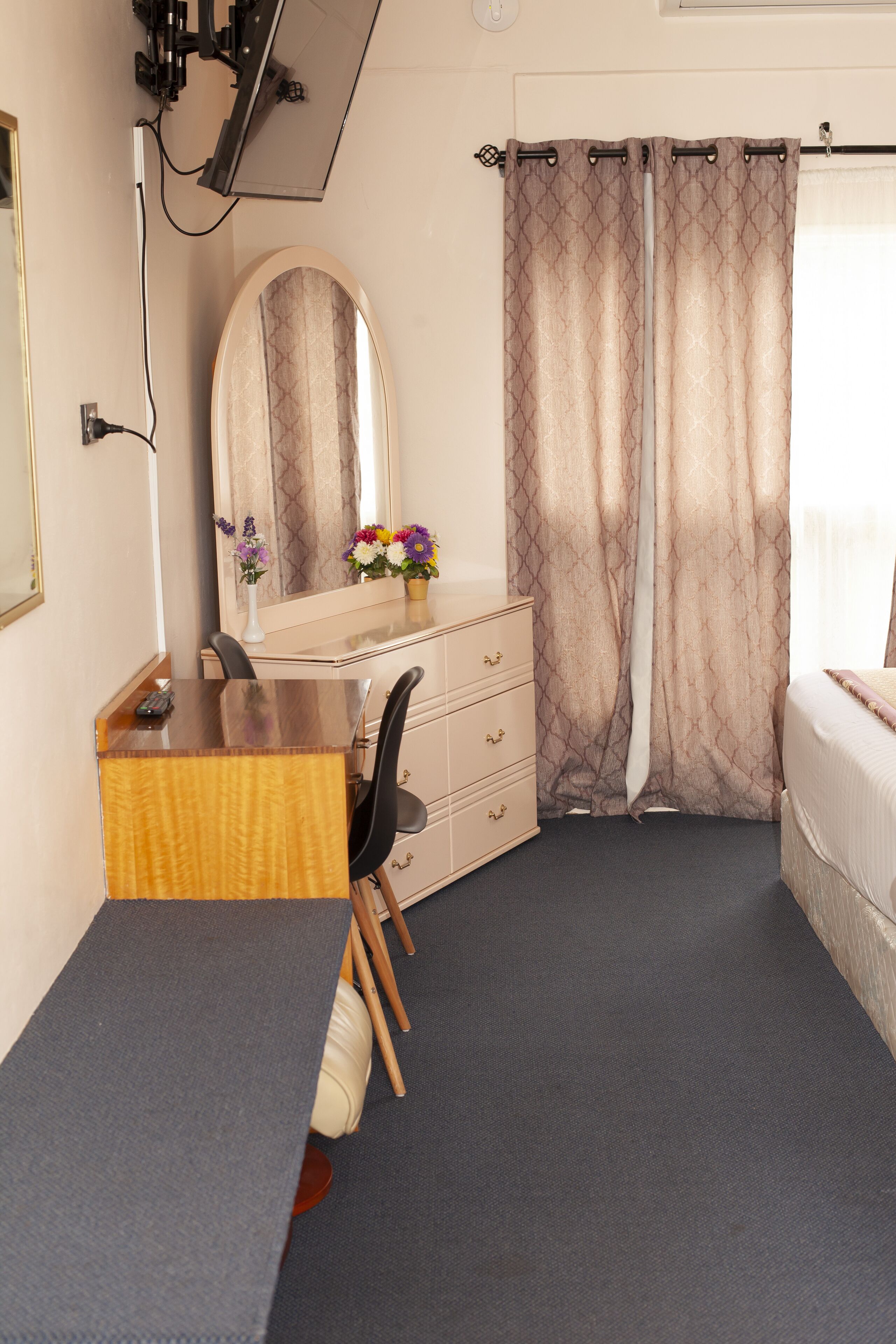 A hotel room with a wooden desk, a mirror, a dresser, and a bed.