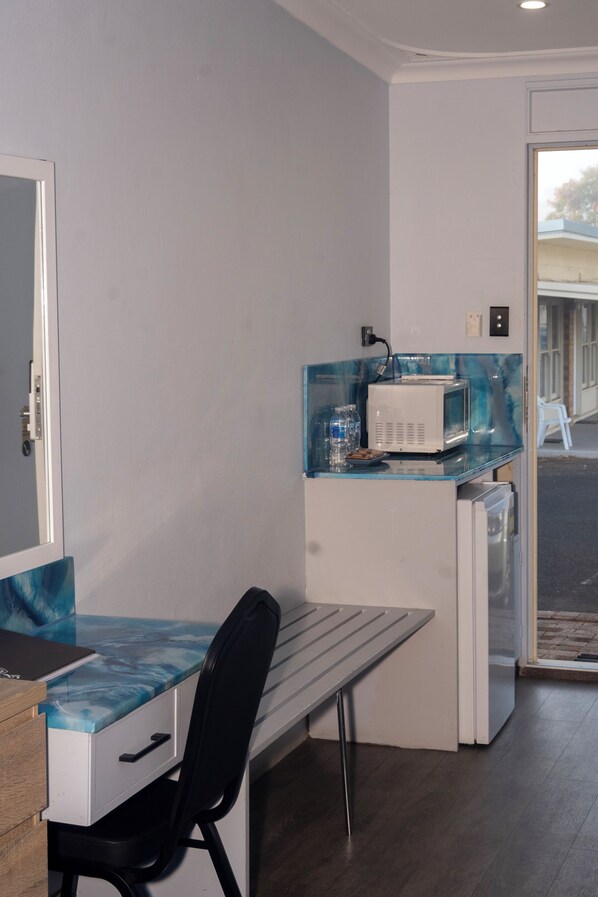 A compact kitchenette with a microwave, a small refrigerator, and a glass-top table.